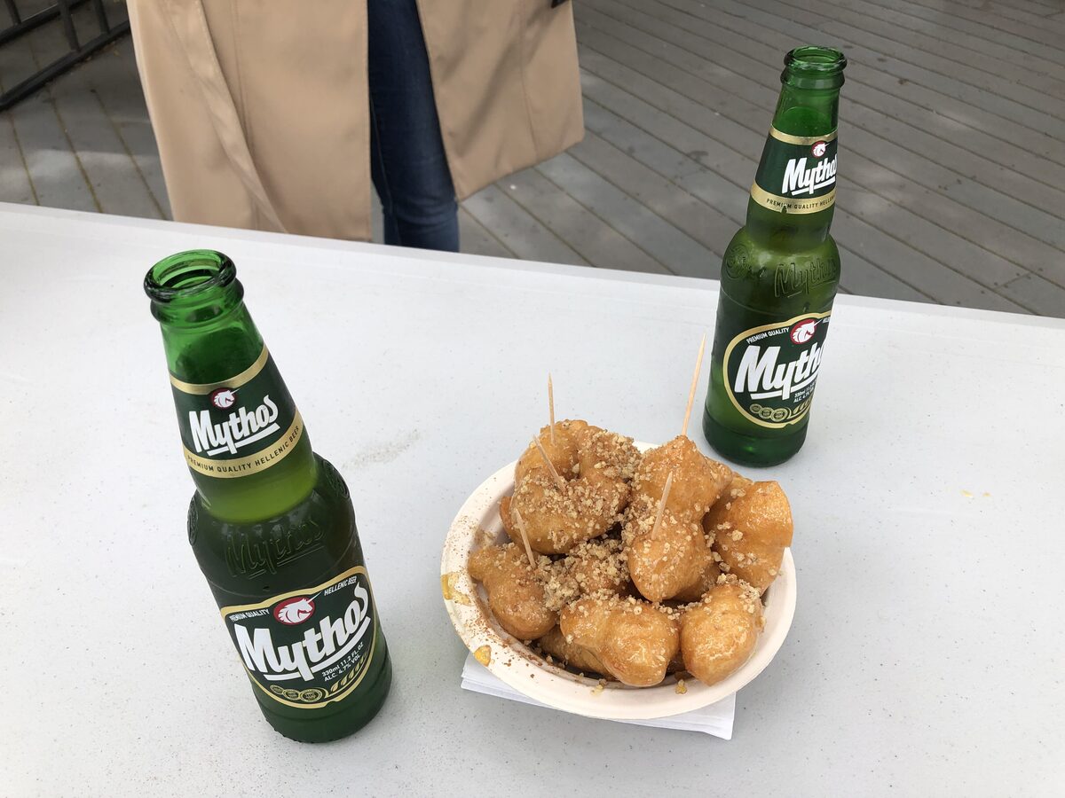 Fried dough balls in a paper cup on a table, next to two bottles of Mythos beer