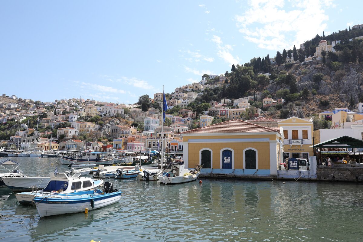 Waterfront houses and fishing boats in the harbor of Gialos, Symi, with a yellow arcaded building on the quay