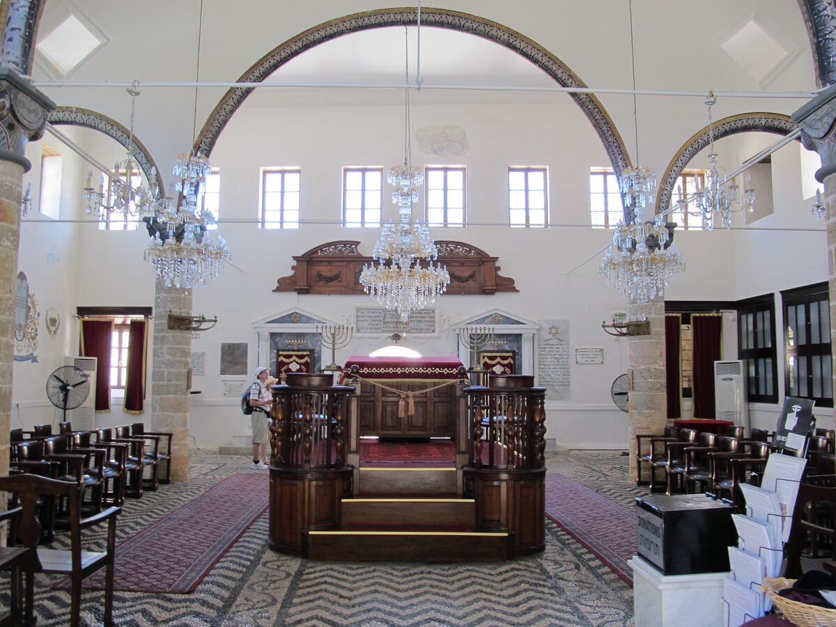 The white interior of Kahal Shalom synagogue with crystal chandeliers and the carved wooden Torah ark