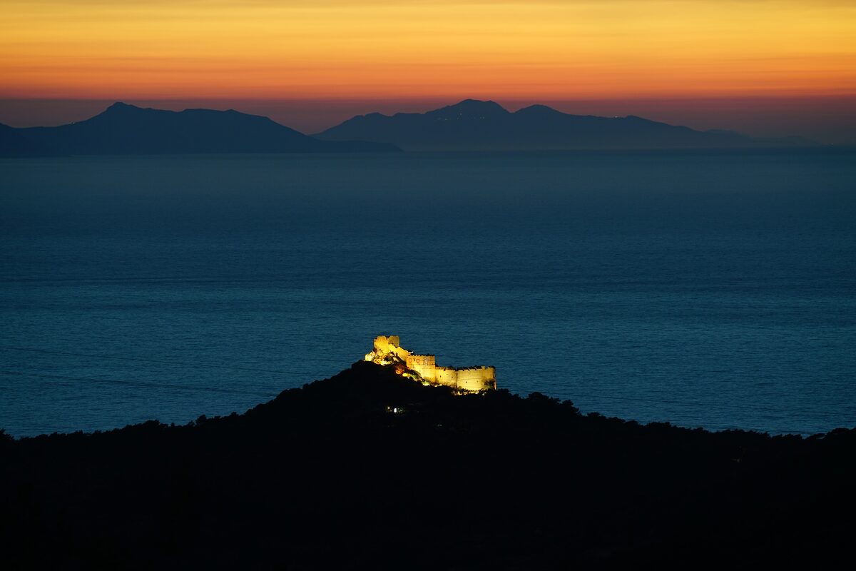 Kritinia Castle lit up on its hill above the dark sea at sunset