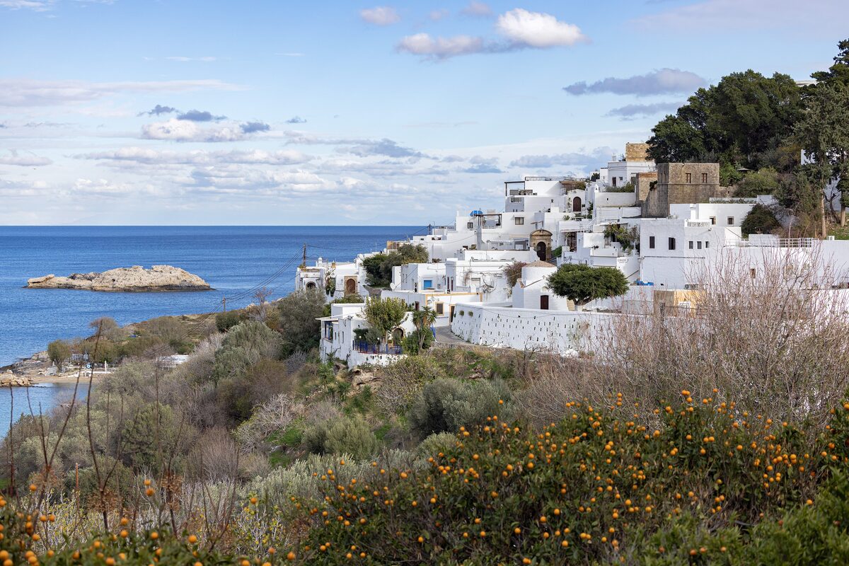 The whitewashed houses of Lindos stacked on the hillside above the bay, with a rocky islet in the sea