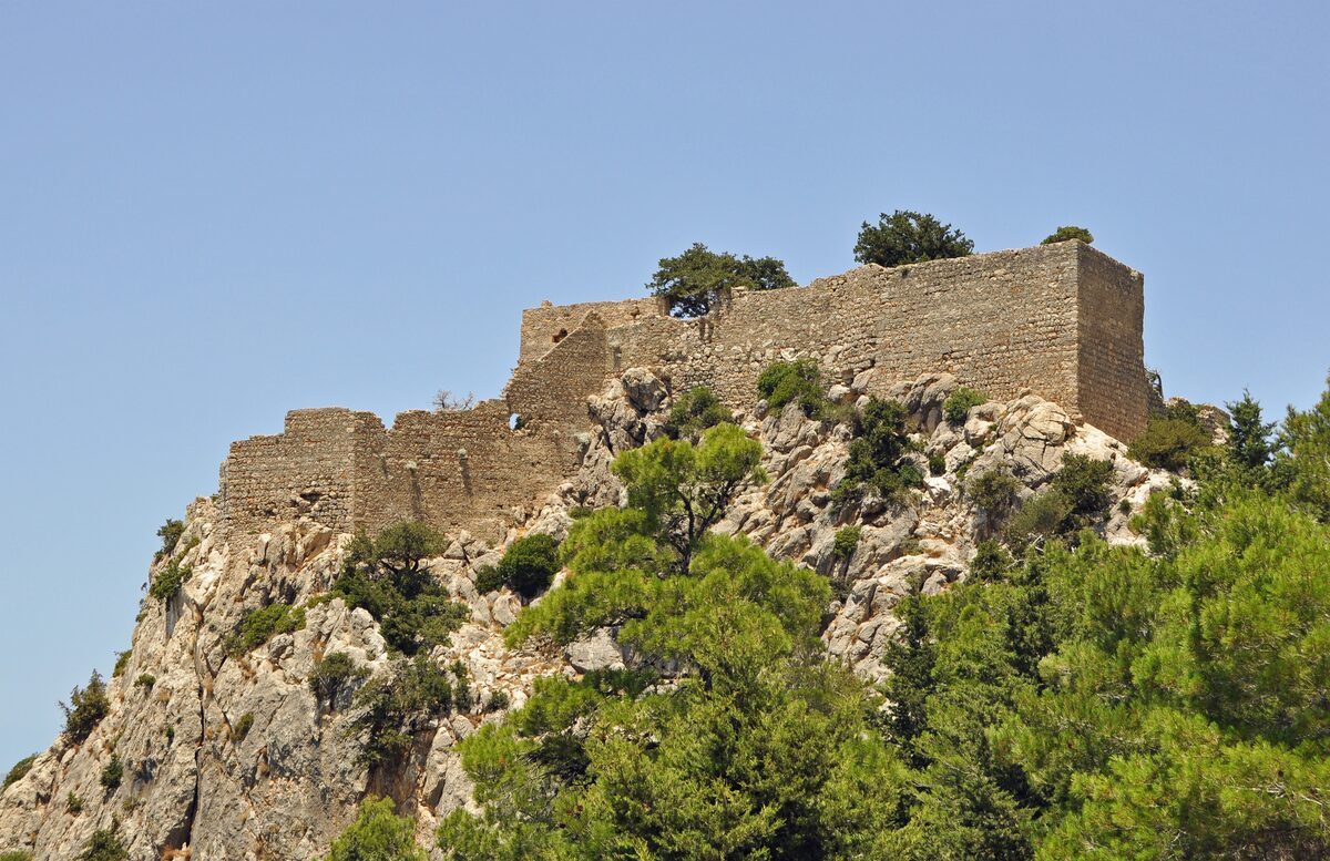 Monolithos Castle's stone walls crowning a steep white rock above the pines, in daylight