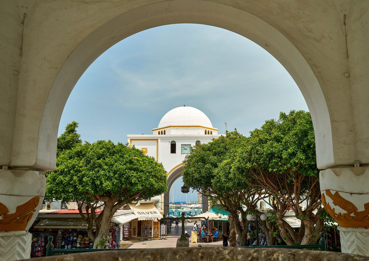 The domed New Market seen through a stone arch, with trees and shop awnings in the courtyard