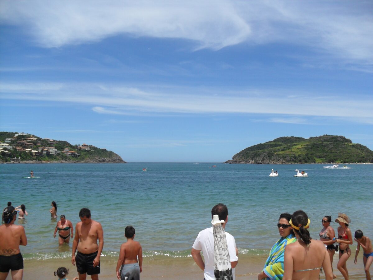 Ferradura beach in Búzios with sand, clear water, people in the shallows and rocky hills around the bay