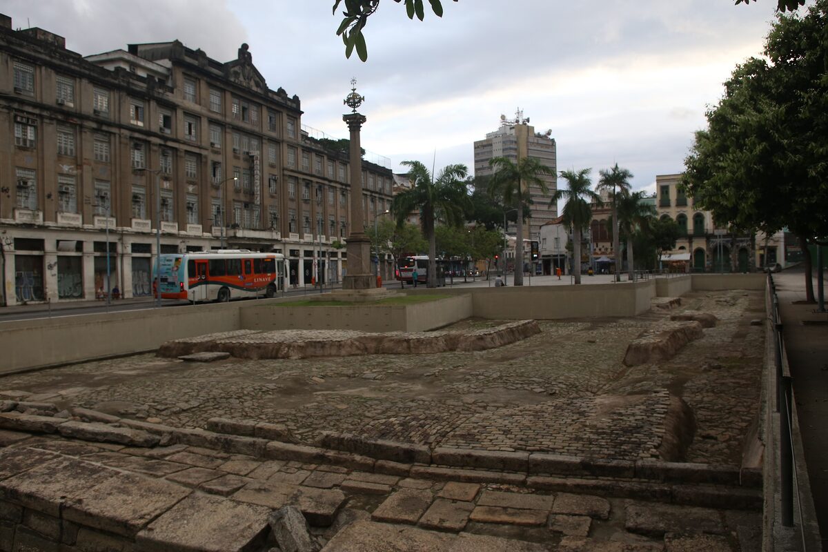 Stone remains of the Valongo wharf on a square with old buildings and palm trees