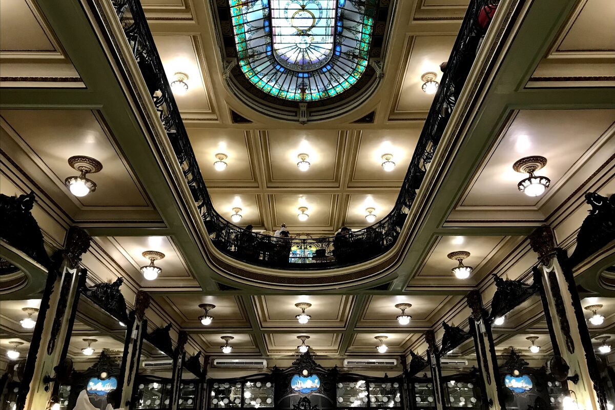 Inside Confeitaria Colombo, with a stained-glass dome, ornate ceiling panels and round ceiling lamps