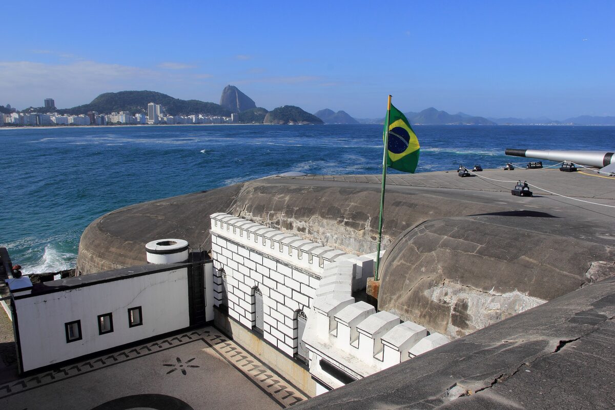 The walls of Forte de Copacabana above the sea, with the Brazilian flag and the Sugarloaf across the bay
