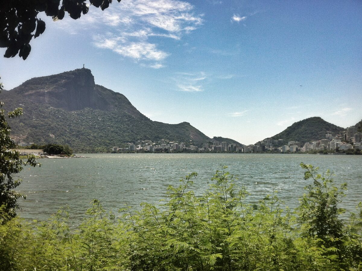 The Corcovado peak with the Christ statue above the Rodrigo de Freitas lagoon in daylight, with green foliage in the foreground