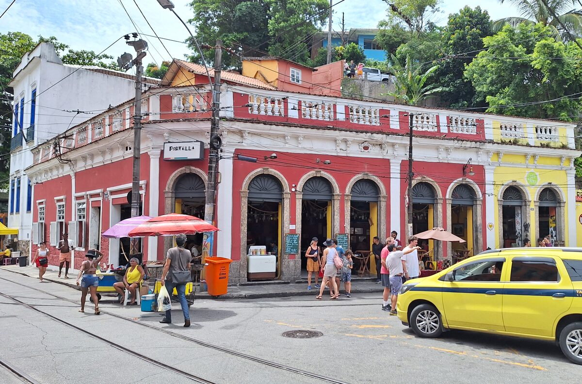 The red and cream colonial building on Largo do Guimarães in Santa Teresa, with a yellow taxi and people at the café tables