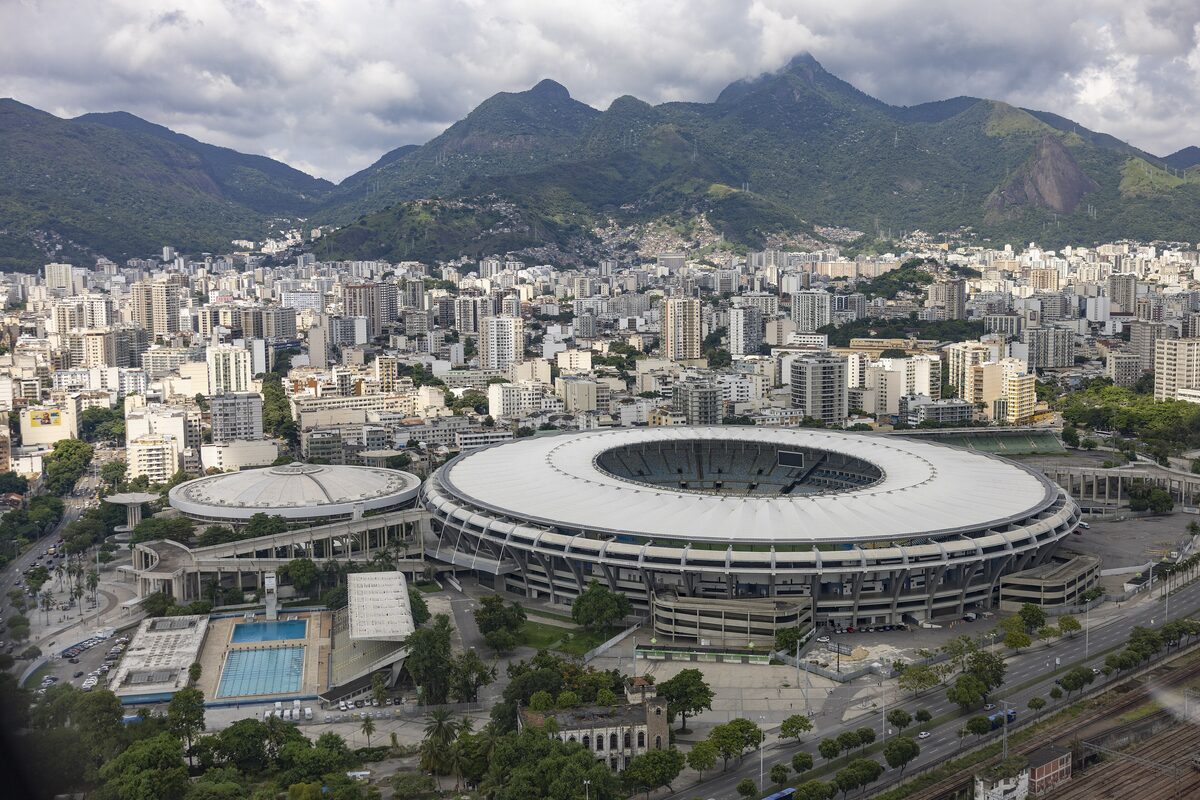 Aerial view of the oval Maracanã stadium with the Maracanãzinho arena beside it, city blocks and green mountains behind