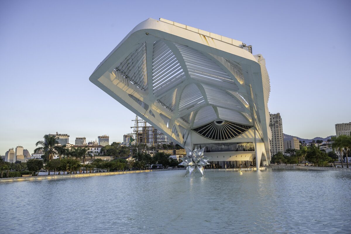 The white, folded Museu do Amanhã building beside the water in daylight, with city towers behind