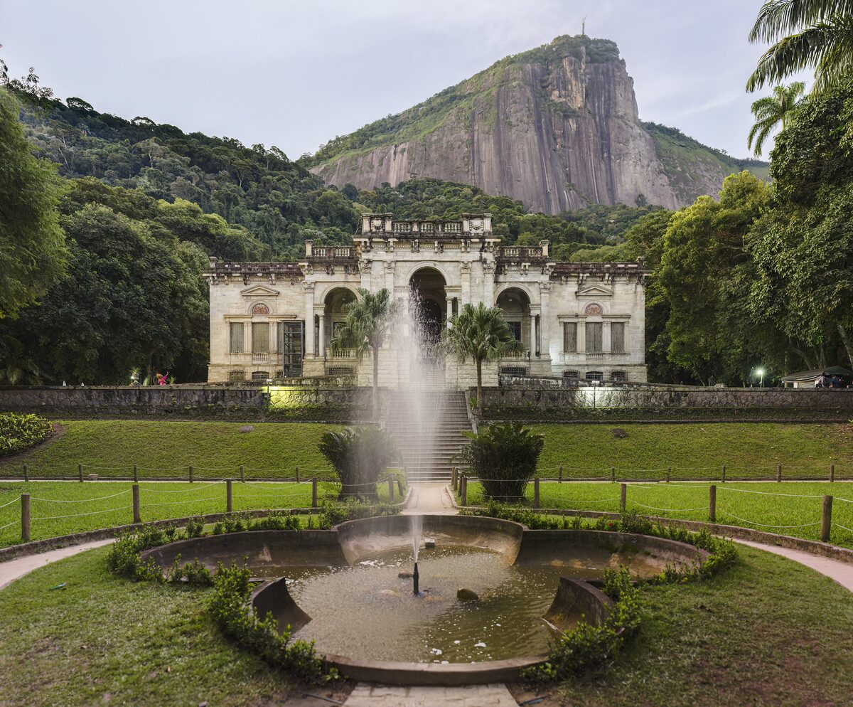 The Parque Lage palace facade over a lawn and fountain, with a mountain rising behind it