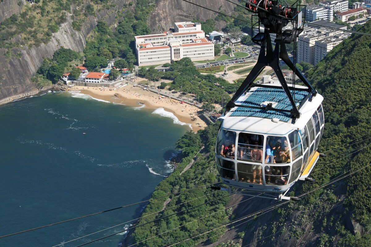 A Sugarloaf cable car climbing over forest, with Praia Vermelha and the bay far below