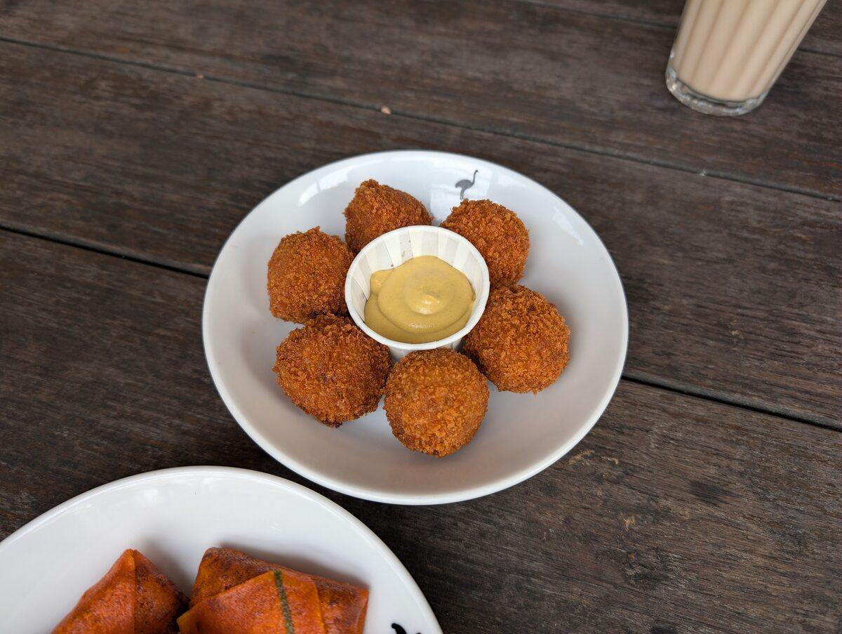A white bowl of golden bitterballen around a small dish of mustard on a wooden table