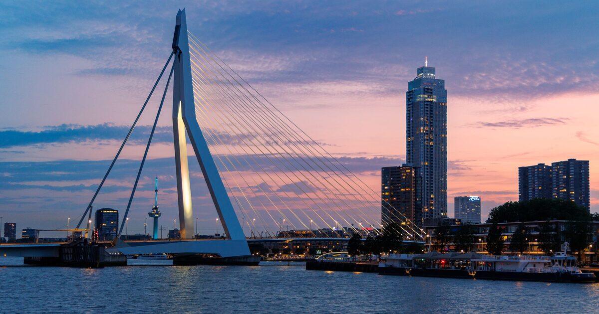 The white Erasmusbrug and the skyline of Rotterdam's riverfront towers against a pink and blue sunset sky over the Maas