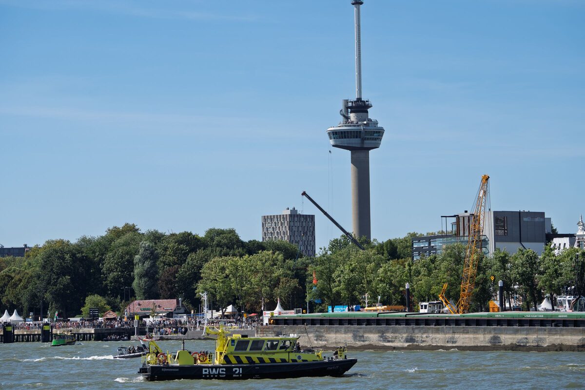 The Euromast tower rising above the trees on the bank of the Maas, with a patrol boat on the river in front