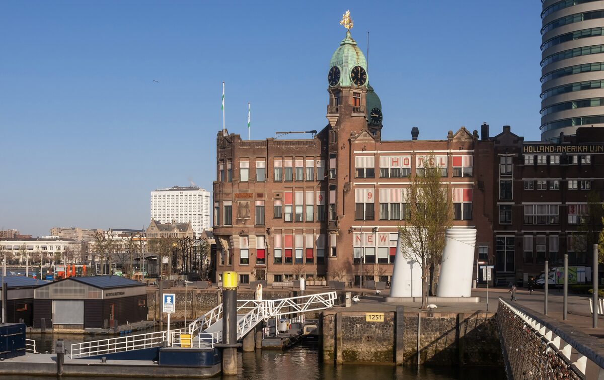 Hotel New York, a red brick building with two green copper towers, at the end of the Wilhelminapier with a modern tower behind it