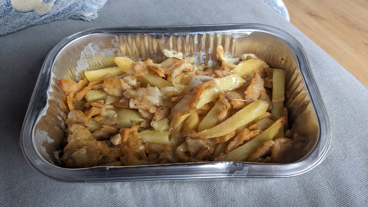 A takeaway tray of kapsalon: fries topped with shawarma meat and melted cheese