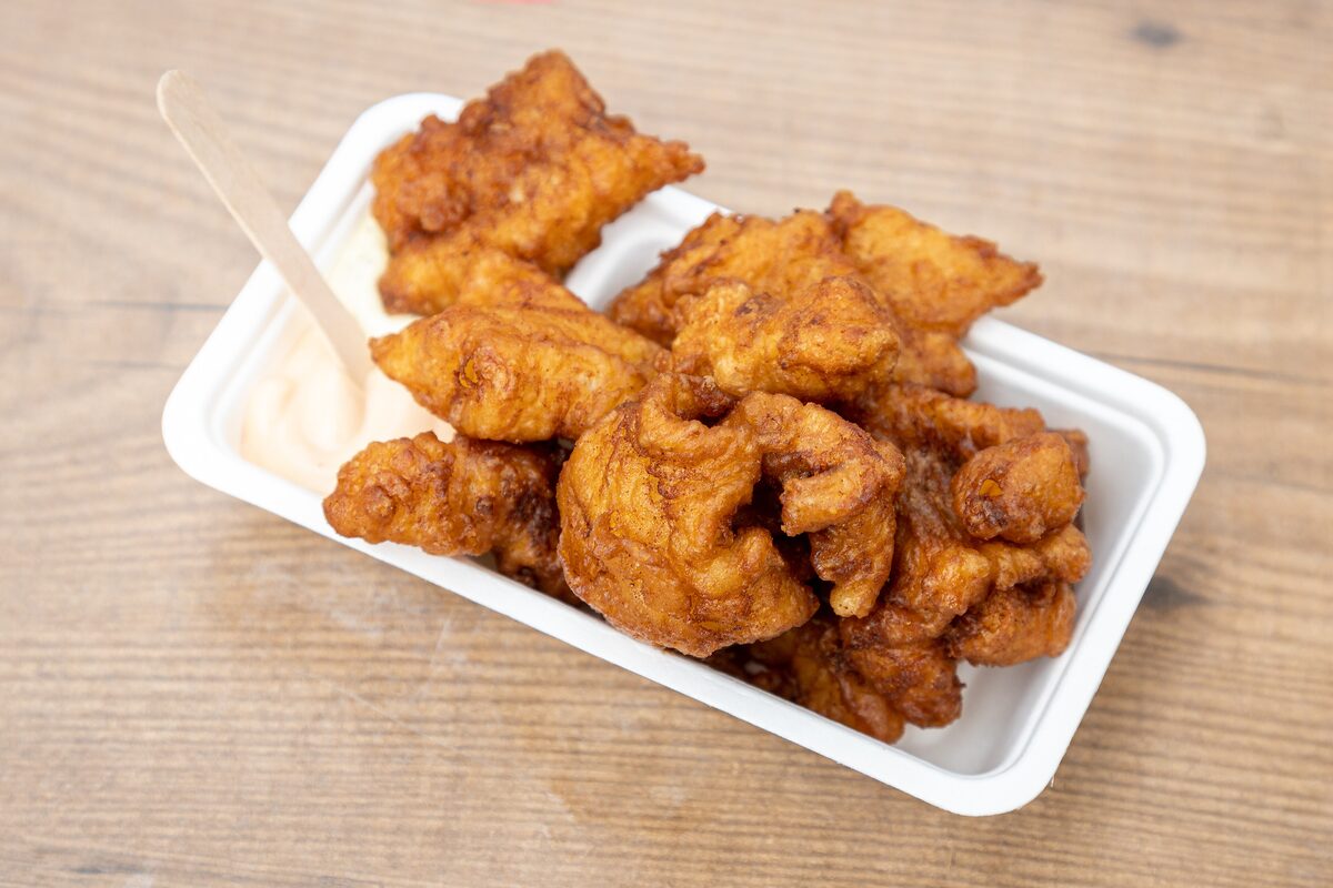 A paper tray of golden fried kibbeling fish pieces with a wooden fork and garlic sauce