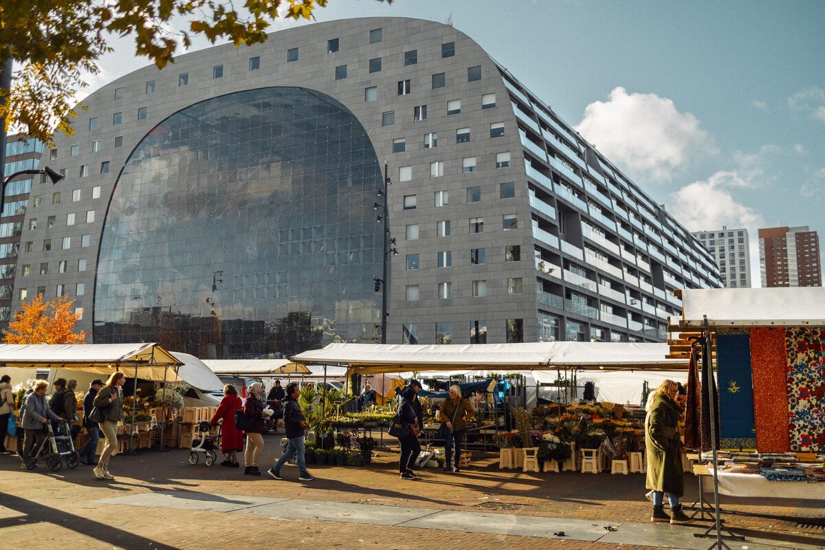 The horseshoe-shaped Markthal with its huge glass end wall, and market stalls with shoppers on the square in front