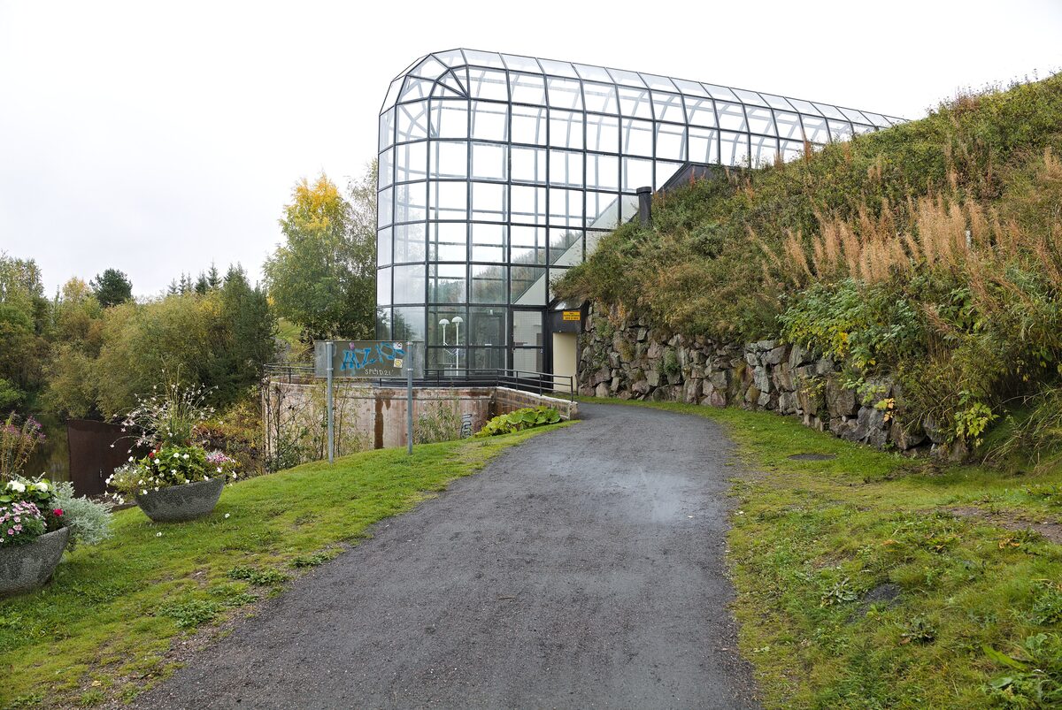 The long glass-roofed corridor of Arktikum emerging from a grassy hillside, with a path leading up to it