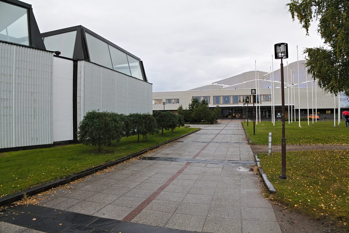 The white Lappia Hall by Alvar Aalto with its tall angled roof windows, beside a paved path and green lawns