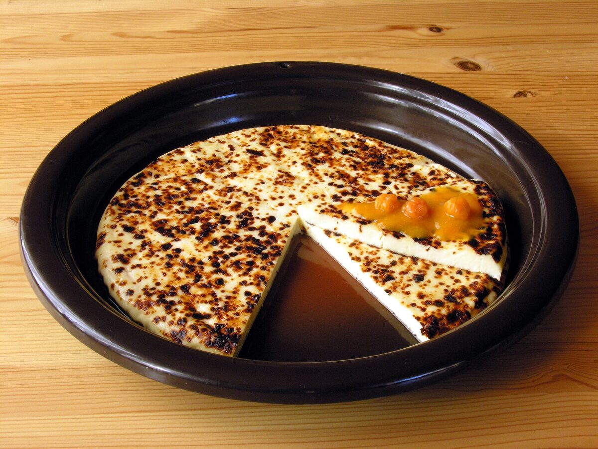 A round of leipäjuusto, baked squeaky cheese with brown spots, with cloudberry jam in a dark dish