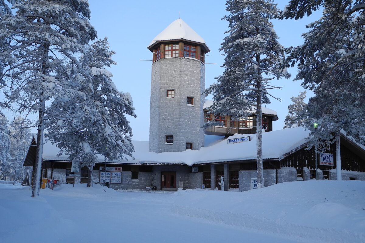 The stone tower and log main building of Ranua Wildlife Park among snow-covered pine trees under a blue sky