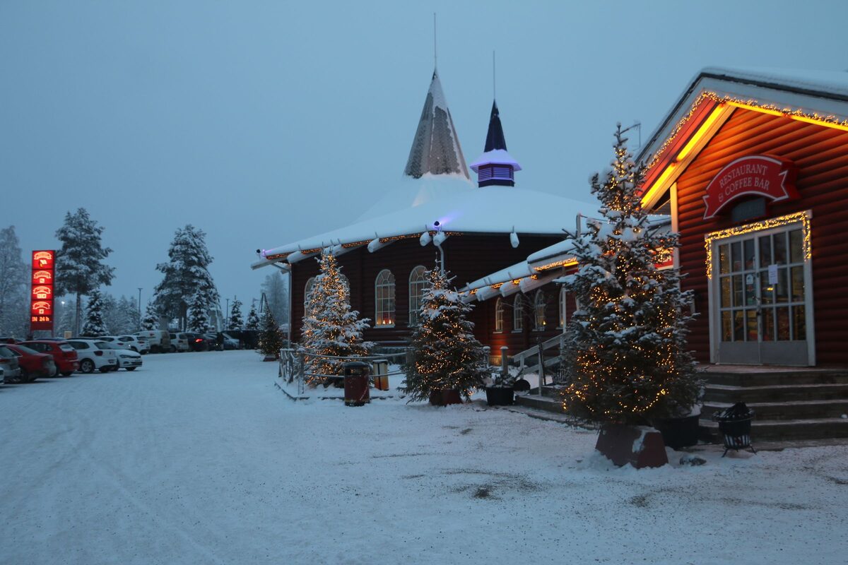 Wooden buildings with pointed roofs, Christmas lights and decorated trees in the snow at Santa Claus Village