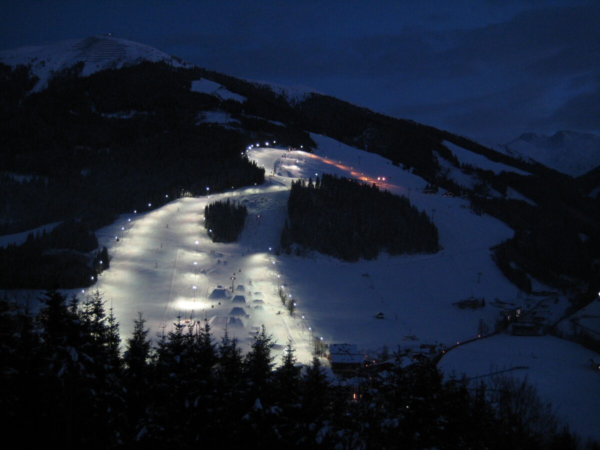 The floodlit night slope on the west side of the Schattberg glowing white against the dark winter hillside above Hinterglemm