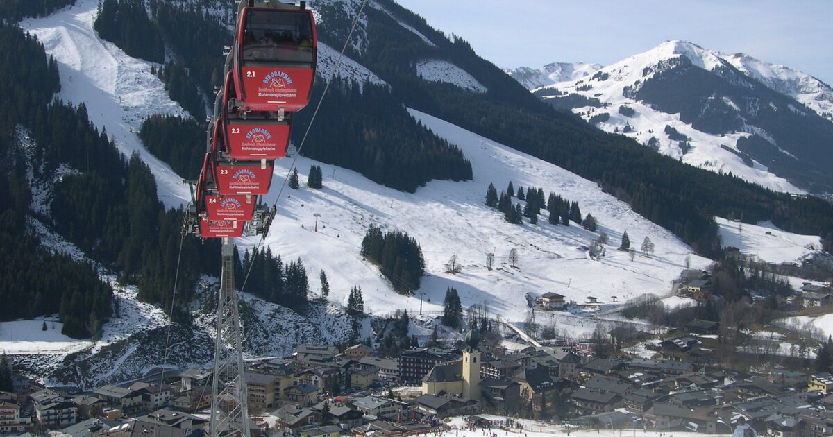Red gondola cabins of the Kohlmaisbahn above Saalbach village, with the church and the snowy slopes in winter sun