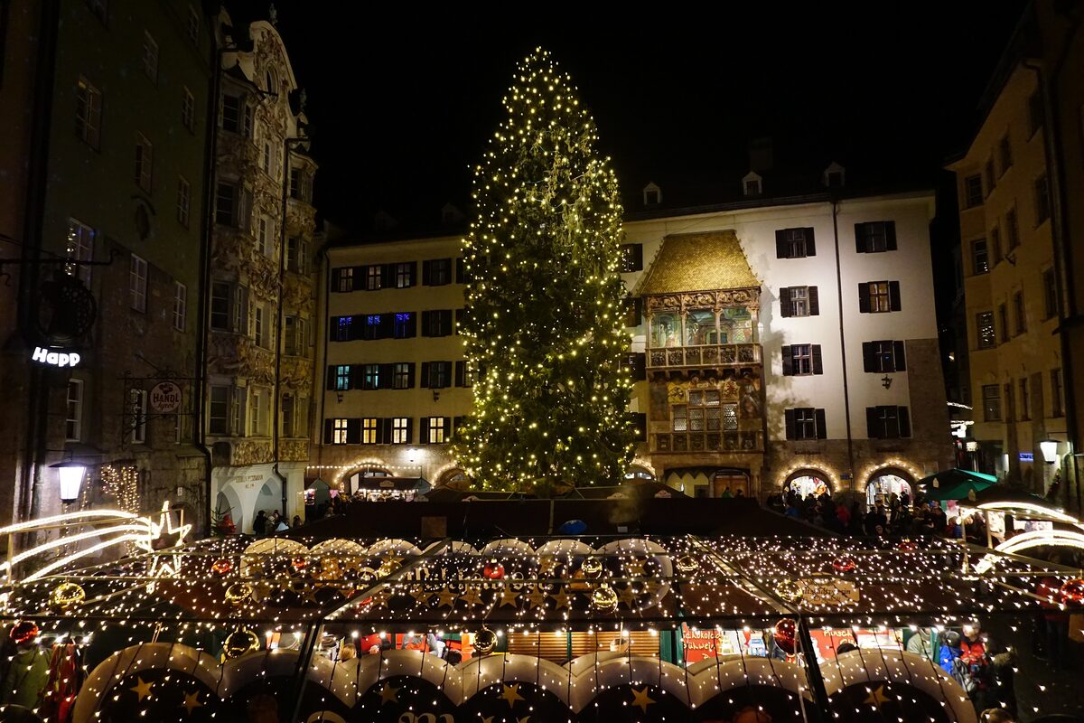 Innsbruck's old town on a December evening, with a lit Christmas tree and market stalls in front of the Golden Roof