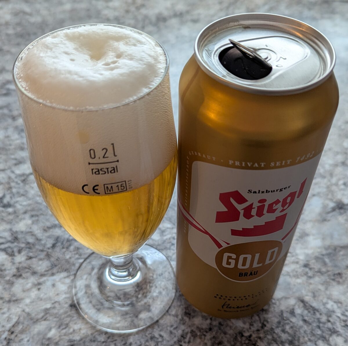 A glass of golden lager beside a can of Stiegl Gold, a Salzburg beer, on a grey stone table