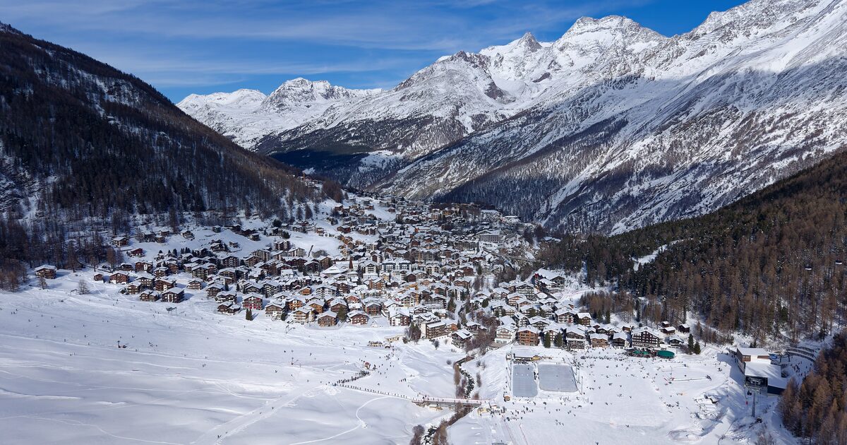 Saas-Fee village in bright winter sun, with snowy peaks rising behind it and a ski slope at its edge