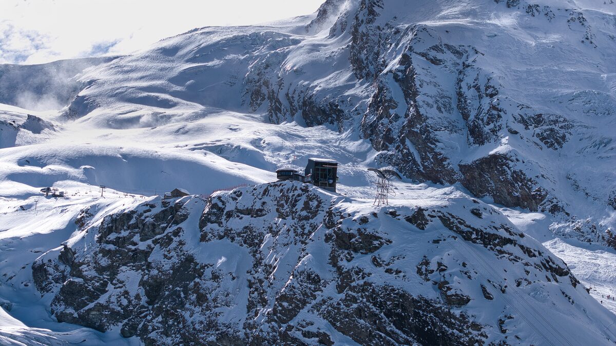 The Längfluh mountain station on a snowy rocky ridge, with glaciers and peaks around