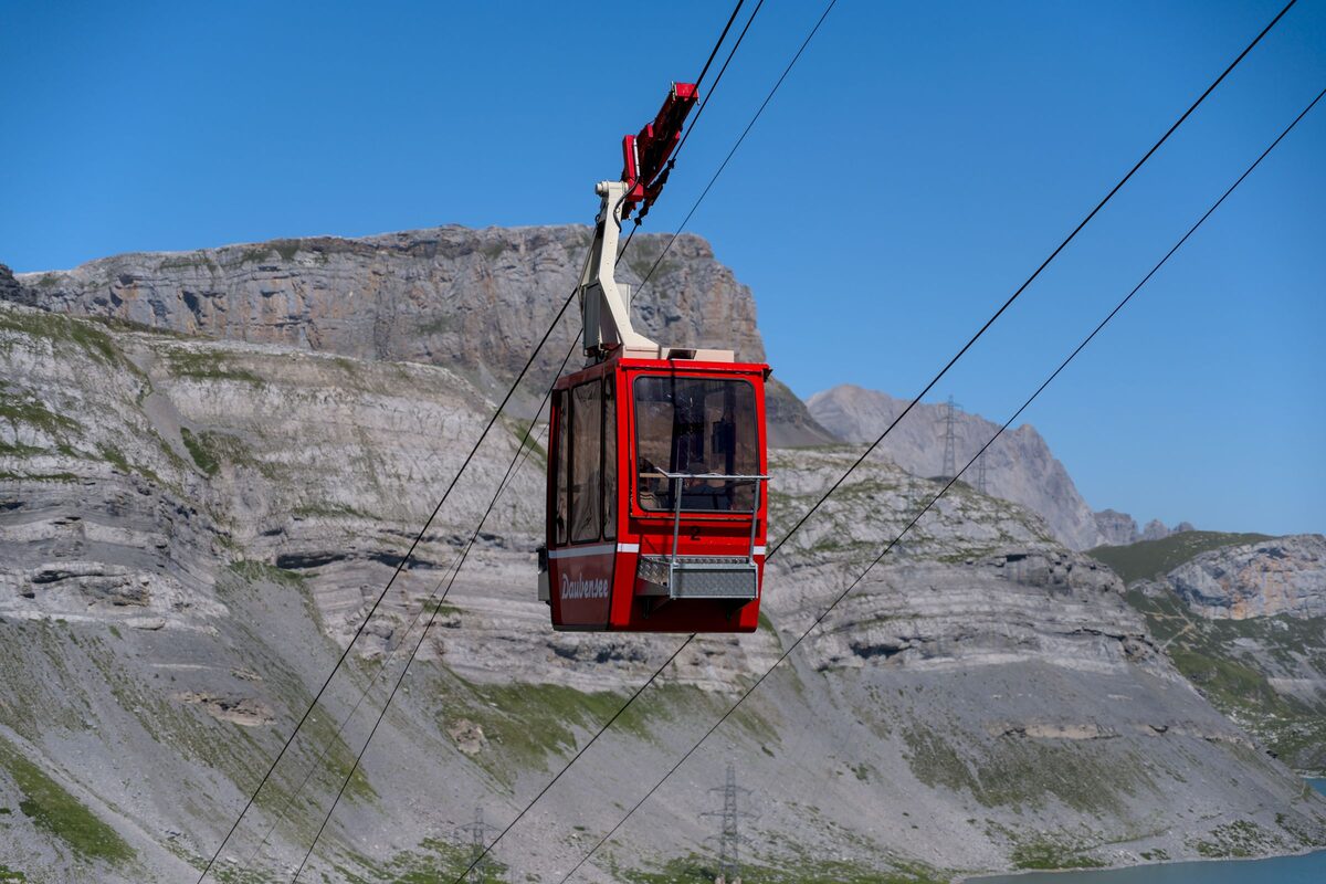A red cable car cabin above rocky Alpine slopes, with a blue sky behind