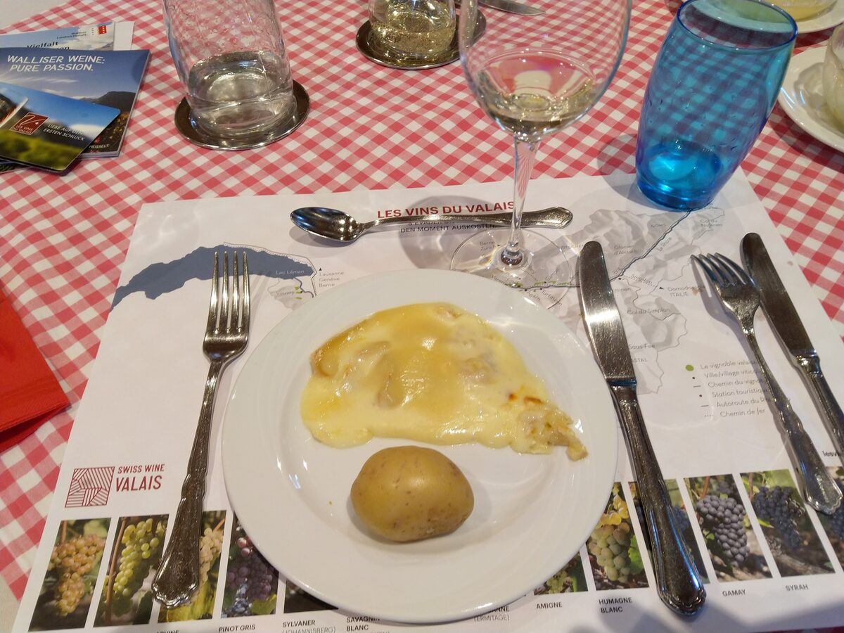 Melted raclette cheese over a boiled potato on a white plate