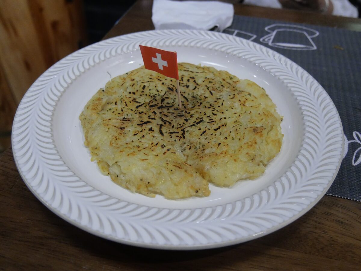 A golden rösti cake on a white plate with a small Swiss flag