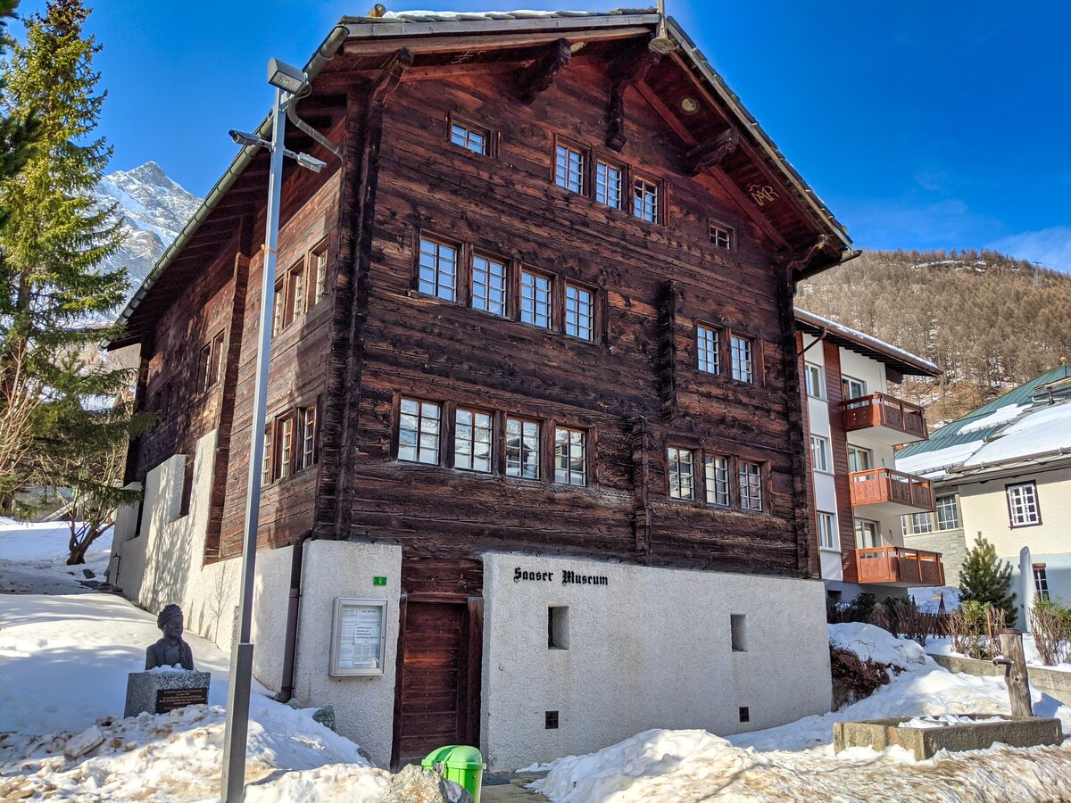 The timber house of the Saas Museum with snow banks along its base