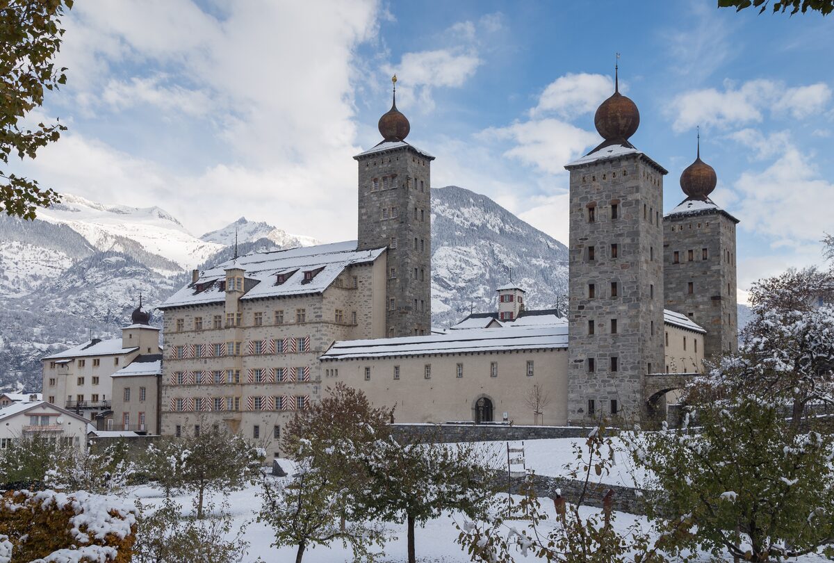 The Stockalper Palace in Brig with its three onion-domed towers, light snow on the roofs and the mountains behind