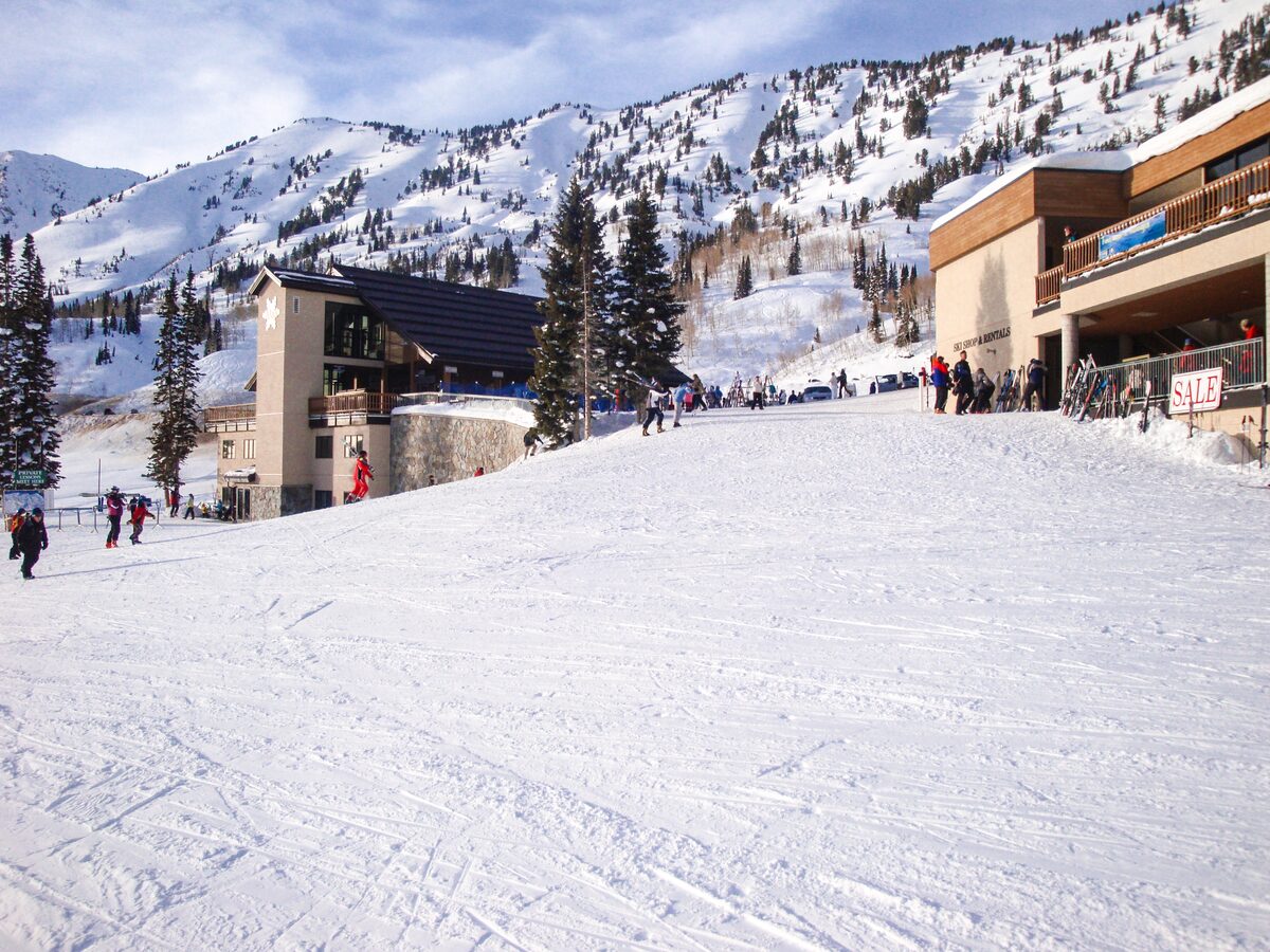 Skiers and two timber lodge buildings at the foot of a wide snowy slope at Alta's Albion Basin