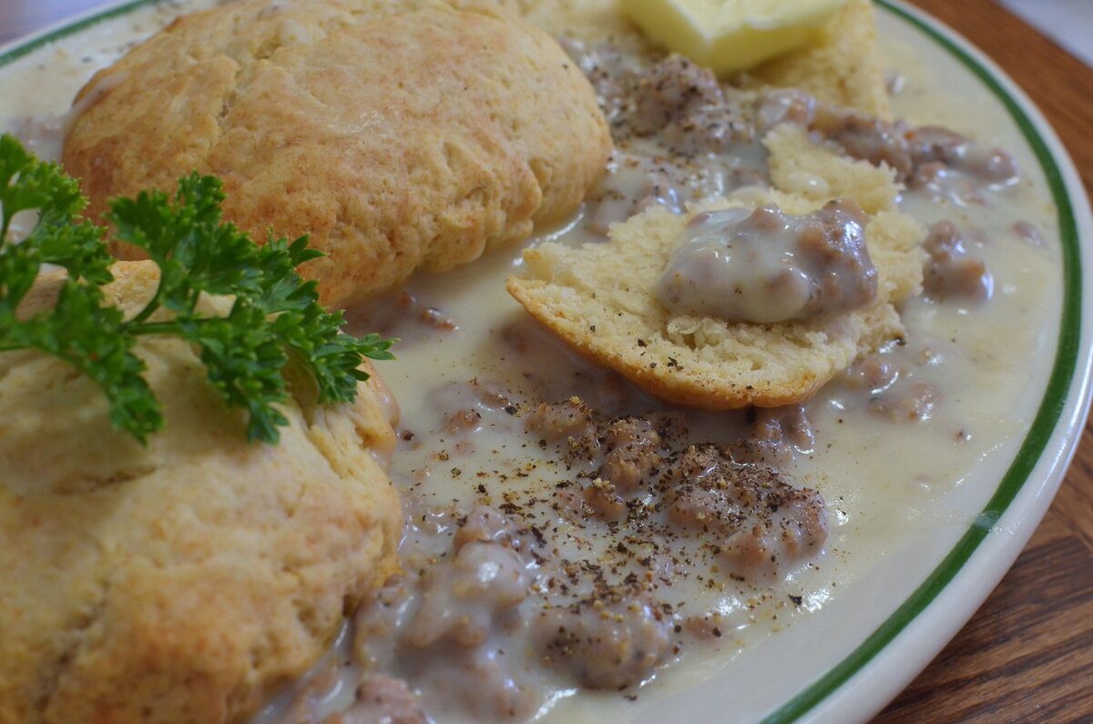 Split buttermilk biscuits on a plate under peppery sausage gravy, with a sprig of parsley