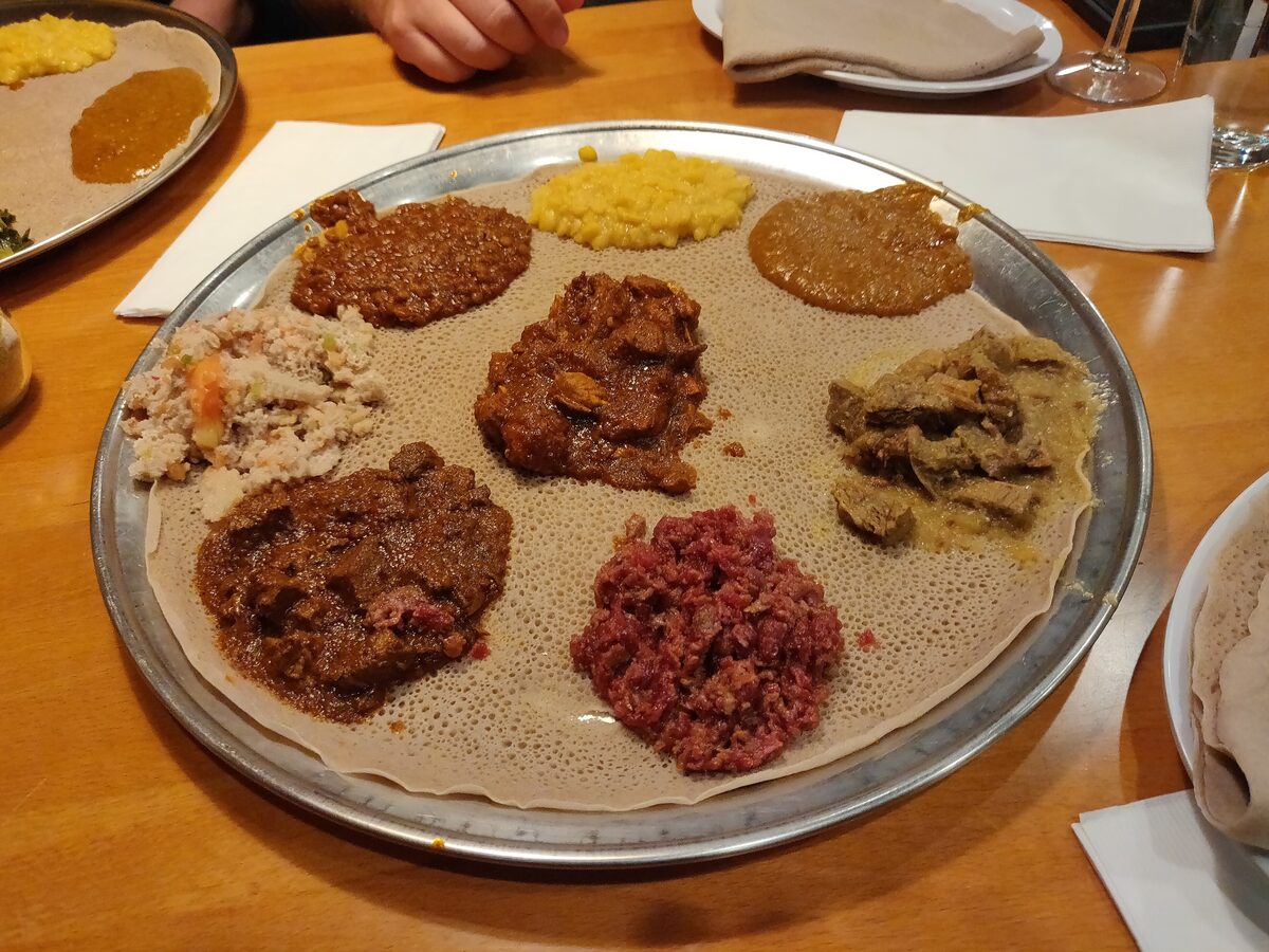 A round metal tray of injera topped with scoops of lentil, beef and vegetable stews