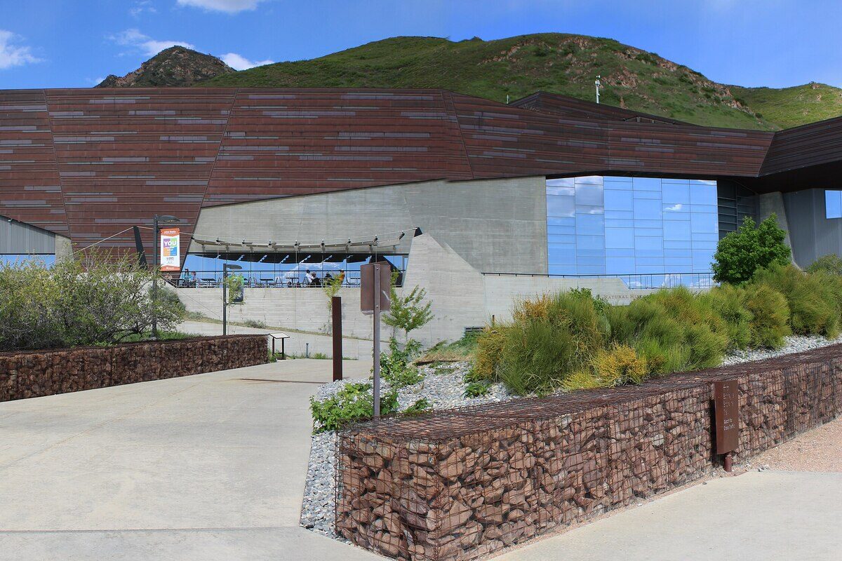 The copper-clad building of the Natural History Museum of Utah with its glass wall and terrace, set against the green foothills of the Wasatch