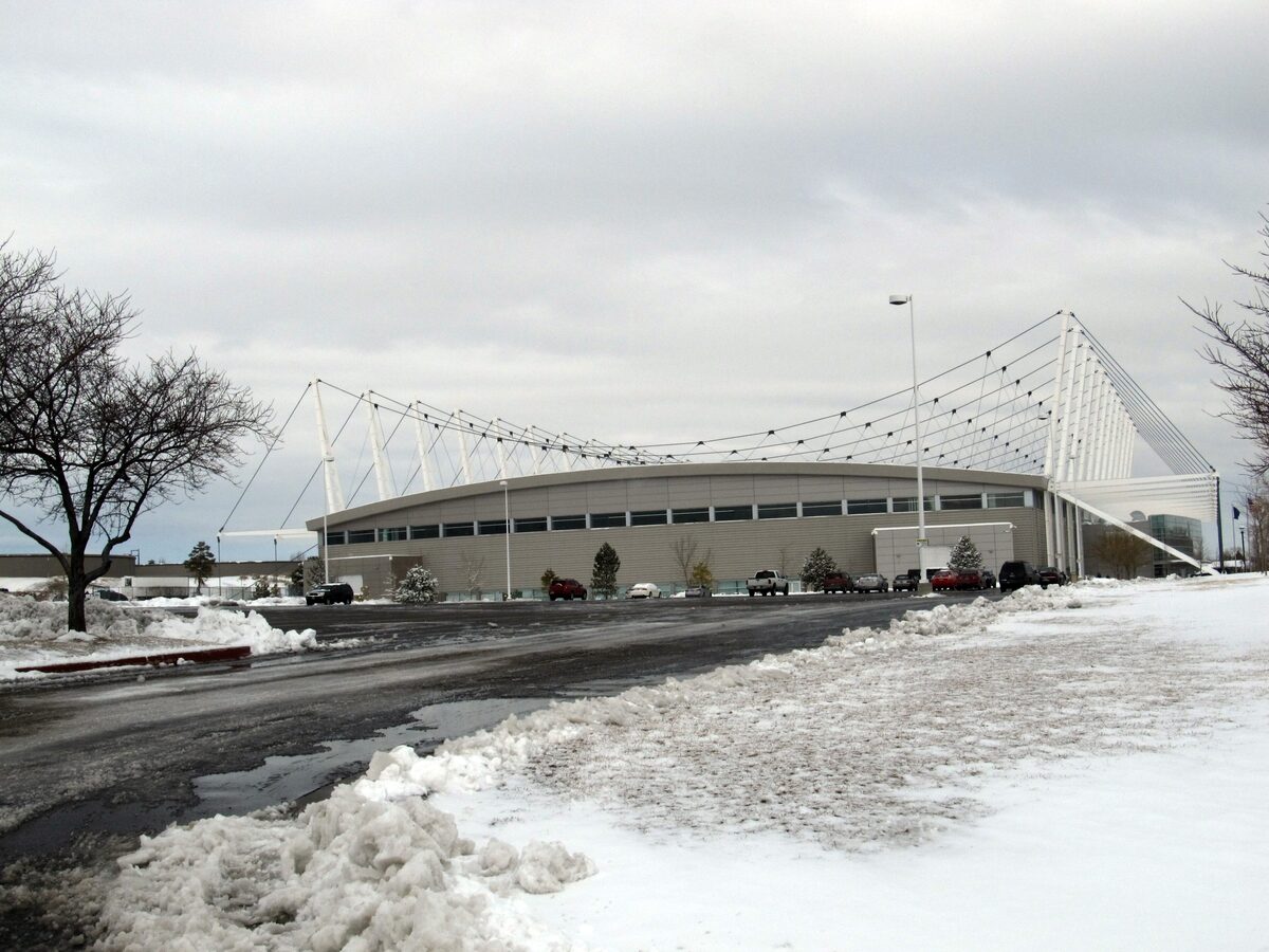 The long Utah Olympic Oval speed-skating hall with its white cable-stayed roof supports, snow banked along the car park