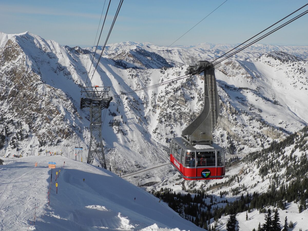 A red Snowbird Aerial Tram cabin climbing its cables above snowy ridges toward Hidden Peak