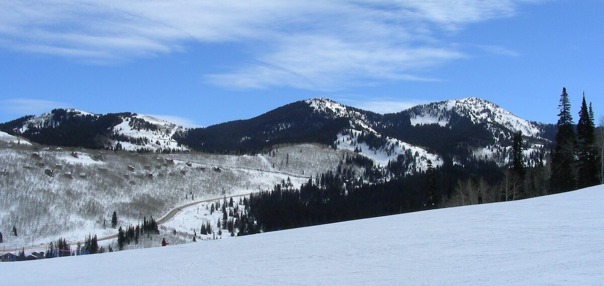 A wide snow slope at Solitude with the forested ridges of Big Cottonwood Canyon and a winding road beyond