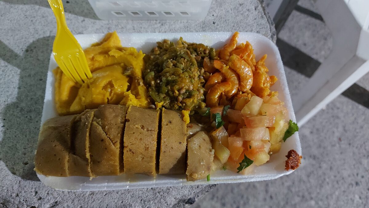 A takeaway plate of Bahian food with sliced abará, yellow vatapá, green caruru and shrimp vinaigrette