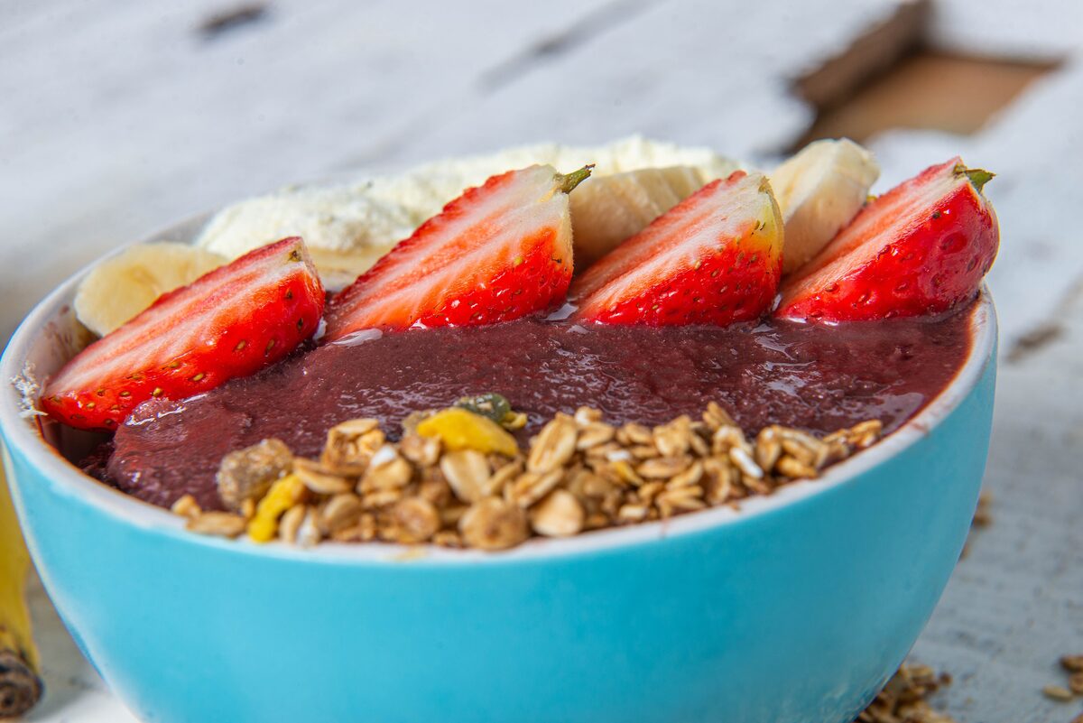 A turquoise bowl of açaí puree topped with strawberry slices, banana, granola and cream