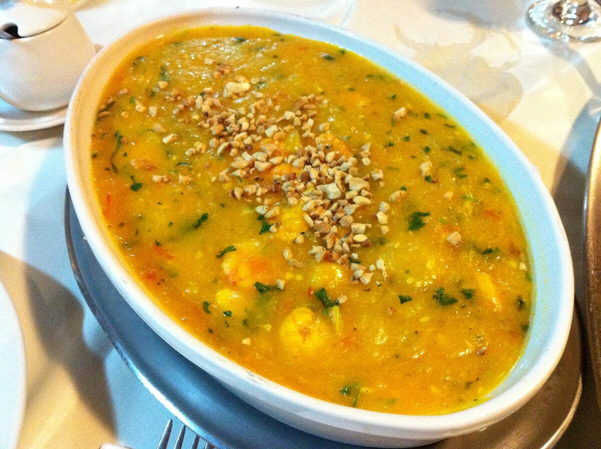 A white oval dish of bobó, a thick yellow-orange stew topped with chopped nuts and herbs